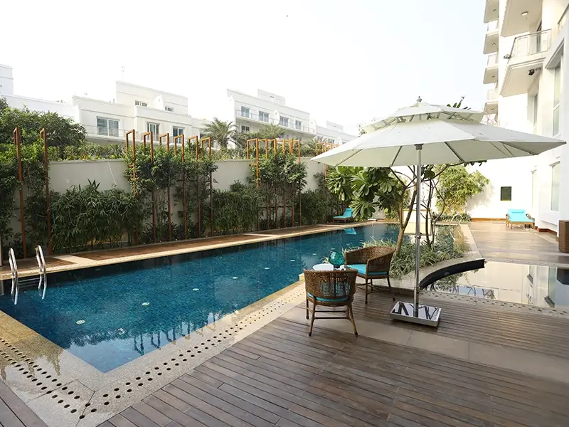 Swimming pool and lounging area, surrounded by comfortable chairs, beautifully landscaped with trees and plants.